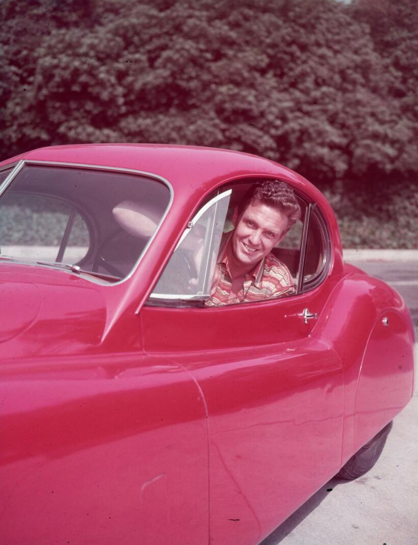 Robert Stack picture taken at the drivers seat of a red automobile in this photo from circa 1955.